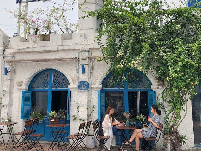 Santorini Vibes Cafe Quán cà phê nằm trên đường Nhật Chiêu lấy cảm hứng từ hòn đảo Santorini nổi tiếng ở Hy Lạp. Quán nổi bật trên nền trời xanh với ngôi nhà trắng, mái vòm xanh, điểm xuyết những tán hoa giấy hồng đỏ rực rỡ. Nội thất quán cũng mang hai màu trắng và xanh da trời, màu sắc đặc trưng của hòn đảo. Ngoài khung cảnh hồ Tây mát mẻ, du khách có thể check-in với những ô cửa hoặc chụp từ đường ven hồ để lấy trọn hình ảnh Santorini thu nhỏ. Giá đồ uống tại đây từ 35.000 - 50.000 đồng. Ảnh: Santorini Vibes Cafe