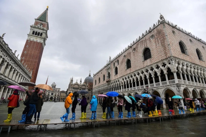 Khách du lịch đi ủng, mang ô tham quan Venice khi thủy triều dâng cao. Ảnh: Miguel Medina/AFP